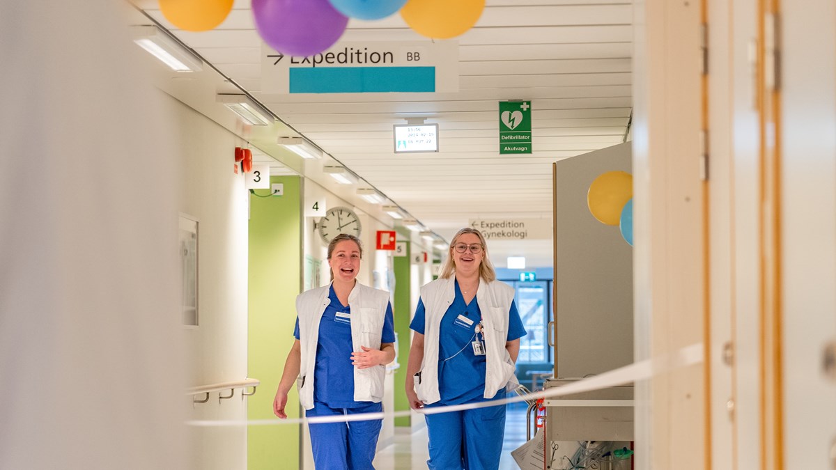 Två kvinnor i sjukhuskläder går i en korridor