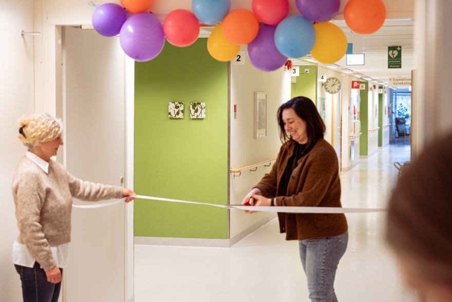 Två kvinnor klipper ett band. Ballonger i taket